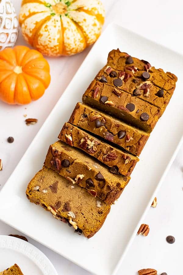 Overhead shot of healthy pumpkin bread recipe cut into slices over a white rectangular plate with pumpkins in the background