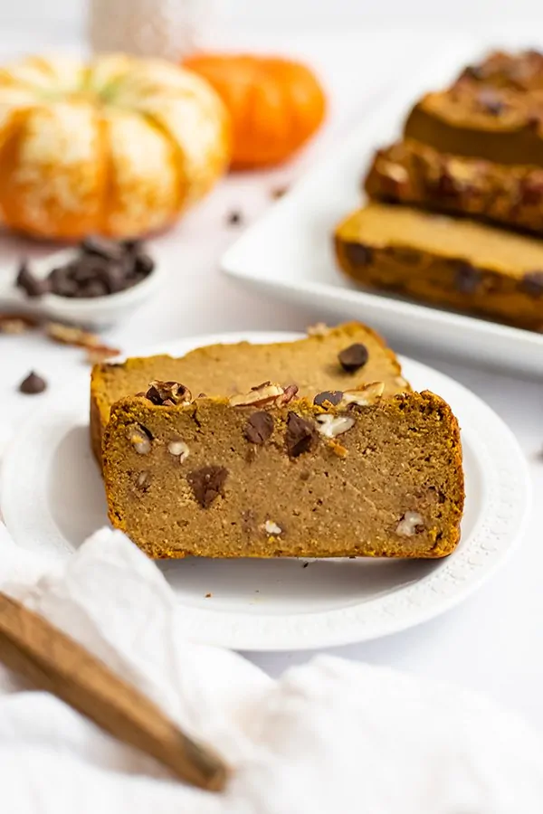 Two slices of healthy pumpkin bread recipe on a white plate with pumpkins in the background