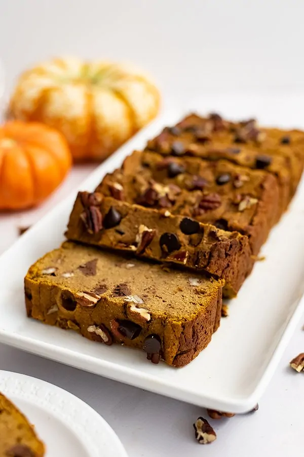 Healthy pumpkin bread recipe cut into slices over a white rectangular plate with pumpkins in the background