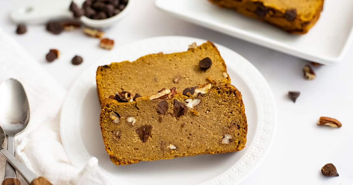 Two slices of healthy pumpkin bread recipe on a white plate with chocolate chips and pecans in the background