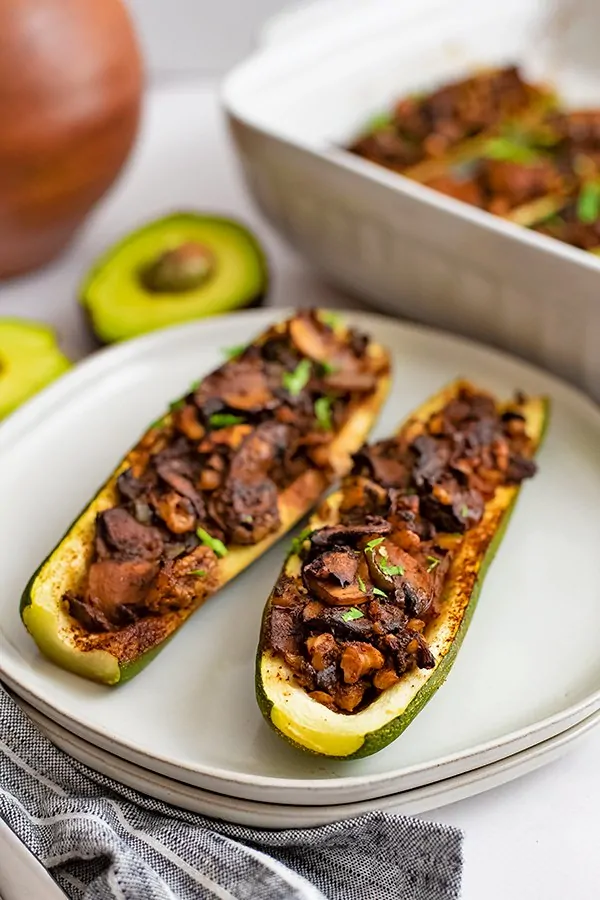 Overhead shot of Two Mexican Stuffed Zucchini Boat Recipe on 2 white plates stacked on top of each other with an avocado in the background