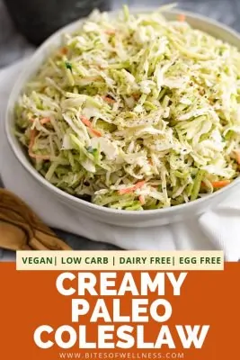 Large white bowl filled with creamy paleo coleslaw on a white napkin with a wooden spoon in the front left of the photo. There is pinterest text on the bottom of the photo