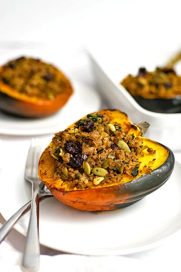 Stuffed acorn squash on a white plate with 2 forks on the plate and a stuffed acorn squash in the background