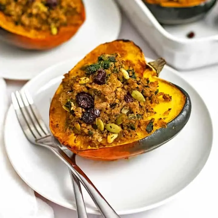 Overhead shot of stuffed acorn squash recipe on a white plate with two forks on the plate with a white serving dish in the background