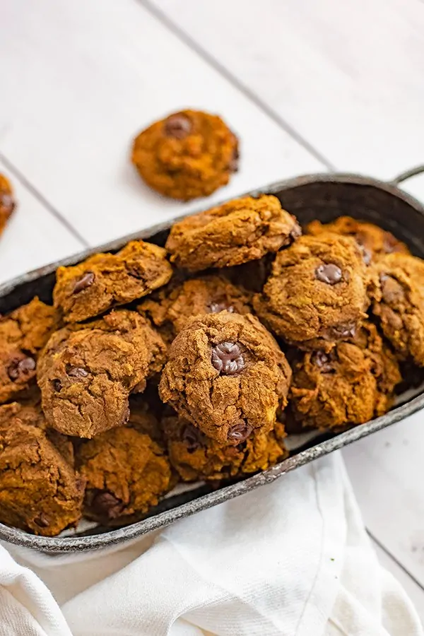 Overhead shot of a silver basket filled with butternut squash chocolate chip protein cookies with a white napkin in the front of the basket