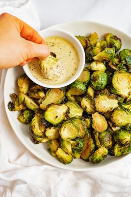 Large plate filled with crispy roasted brussel sprouts with garlic dijon sauce with a brussel being dipped into the sauce