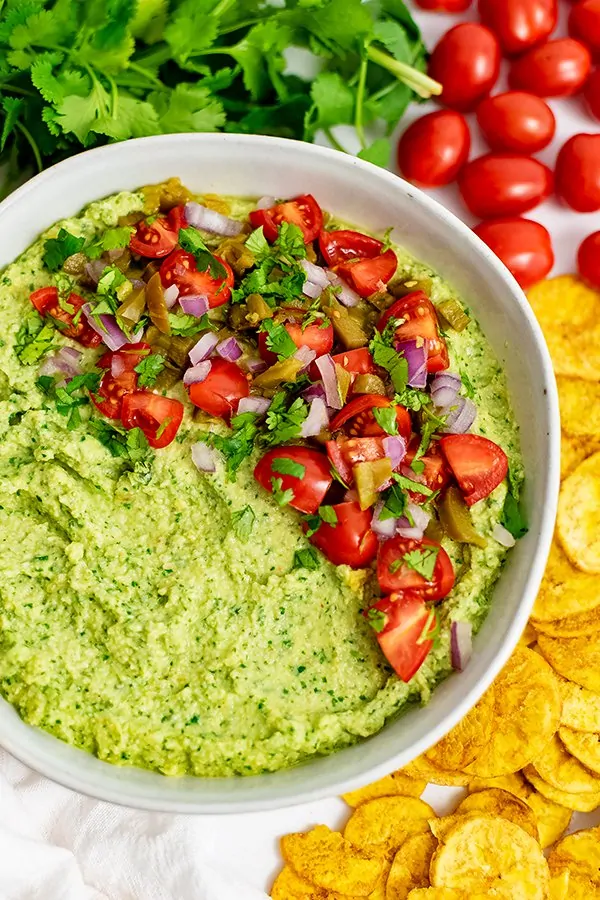 Overhead shot of jalapeno cilantro hummus with plantains, cherry tomatoes and cilantro around the bowl.