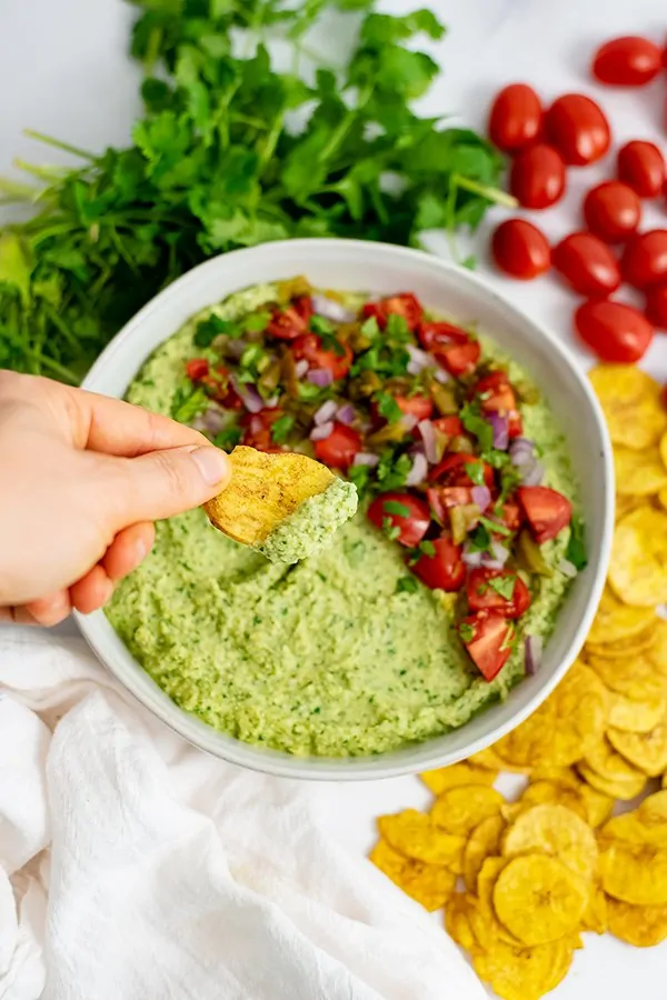 Overhead shot of bowl filled with jalapeno cilantro hummus with a plantain chip dipping into the hummus.