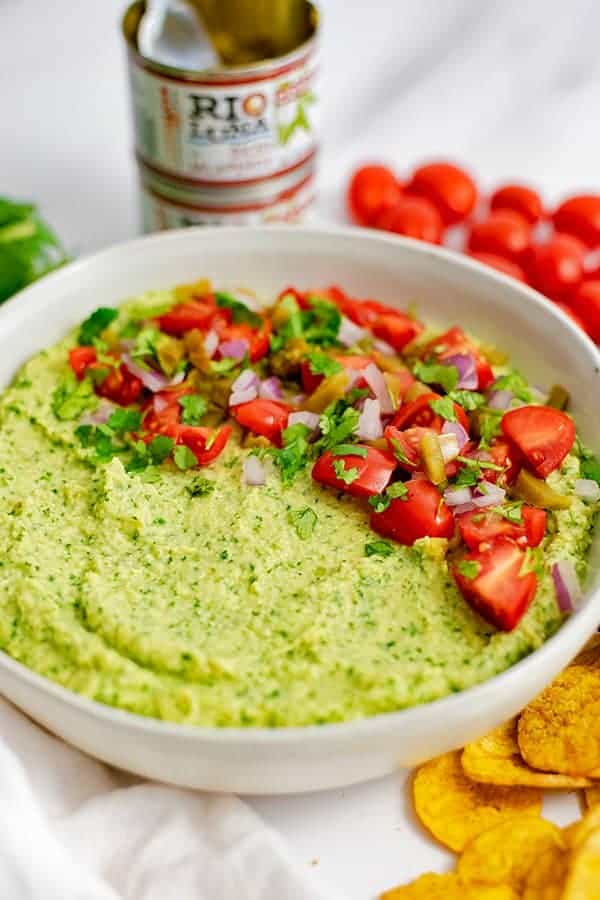 Large white bowl filled with jalapeno cilantro hummus with cans of Rio Luna Diced Jalapenos in the background