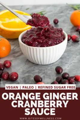 Bowl of orange ginger cranberry sauce with oranges in the background and cranberries around the bowl. Pinterest text on the bottom