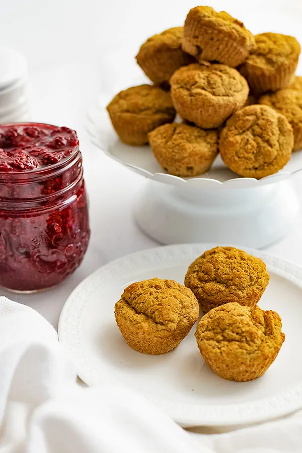 Gluten free almond flour muffins on a white plate with a jar of raspberry jelly in the background