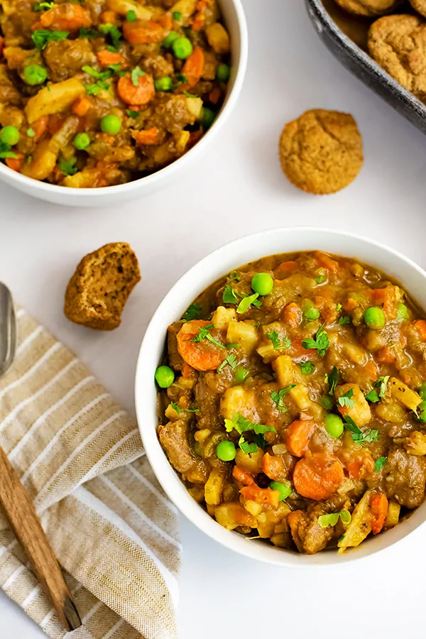 Overhead shot of two bowls of easy beef stew (instant pot recipe) with almond flour muffins between the bowls and a brown striped napkin to the left.