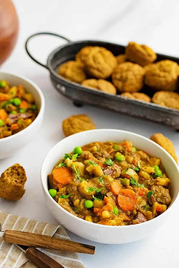 White bowl filled with easy beef stew (instant pot recipe) with a basket of almond flour muffins in the background.