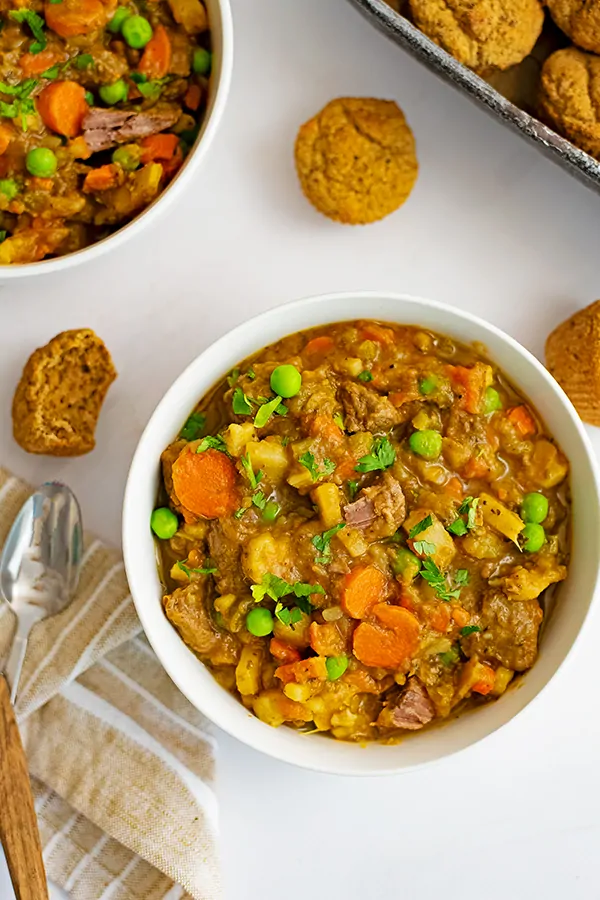 Overhead shot of white bowl filled with easy beef stew (instant pot recipe) with a spoon with a wooden handle on a brown striped napkin to the left.