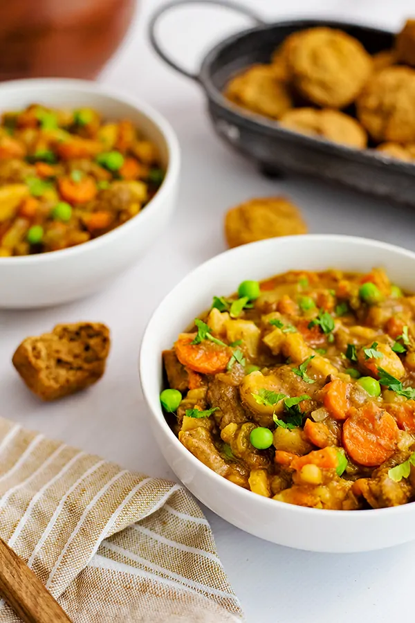 Two white bowls filled with easy beef stew (instant pot recipe) with a basket of almond flour muffins in the background