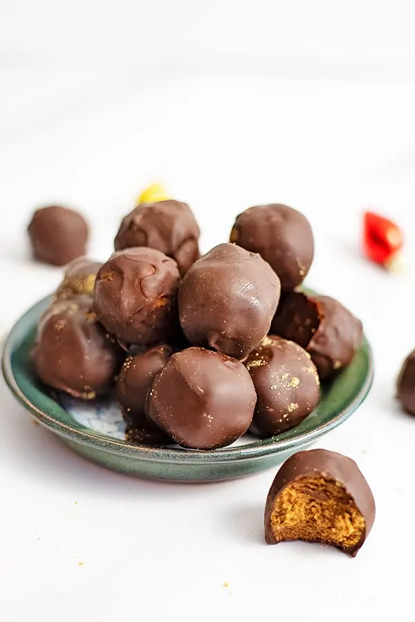 Small green plate filled will gingerbread truffles with a gingerbread truffle with a bite removed in front of the plate.