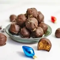 Small green plate filled will gingerbread truffles with a gingerbread truffle with a bite removed in front of the plate. The plate is surrounded by holiday decorations