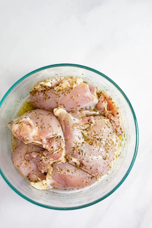 Glass bowl filled with raw chicken thighs in the greek chicken marinade