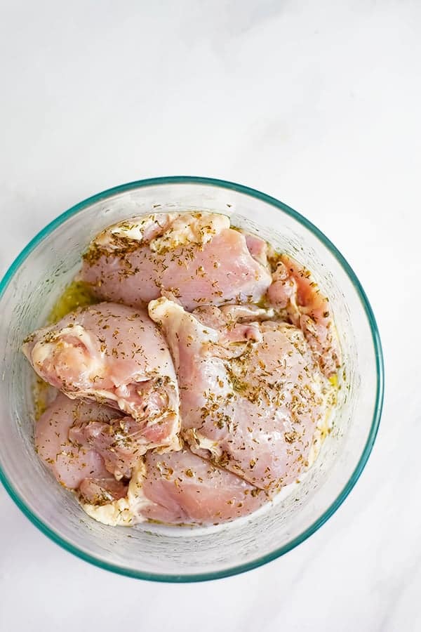 Glass bowl filled with raw chicken thighs in the greek chicken marinade 