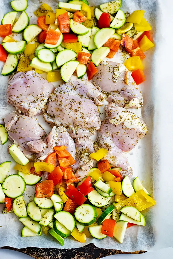 Greek Chicken Marinade Sheet Pan Dinner before the oven. Raw chicken and veggies on a parchment paper lined baking sheet