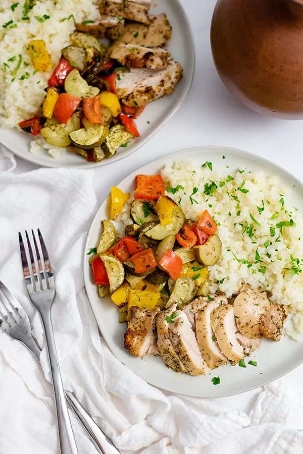 White plate filled with greek chicken marinade sheet pan dinner with two forks next to the plate over a light brown striped napkin