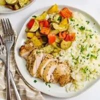 Overhead shot of white dish filled with greek chicken marinade with two forks on the left of the plate over a brown napkin