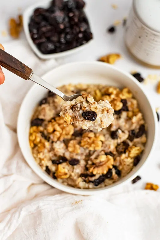 White bowl filled with Walnut Cranberry High Protein Oatmeal with a spoon with a wooden handle hovering over the bowl with a scoop of oatmeal in the spoon