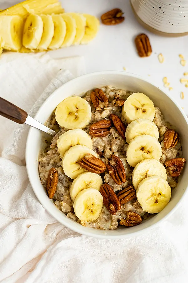 White bowl filled with Banana Nut High Protein Oatmeal with a spoon with a wooden handle in the oatmeal