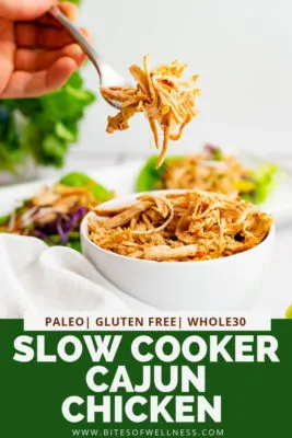 Bowl of Whole30 slow cooker cajun chicken with a hand holding a fork full of the cajun chicken above the bowl. Pinterest text on the bottom of the photo
