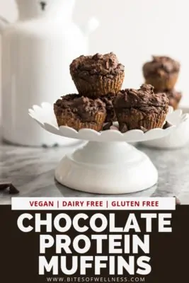 Vegan chocolate protein muffins stacked on top of each other on a cake pedestal with pinterest text on the bottom of the photo
