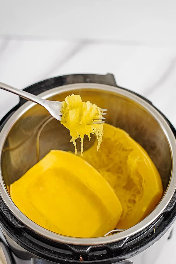 Pressure cooker filled with spaghetti squash. Fork taking strands of spaghetti squash from the Instant Pot