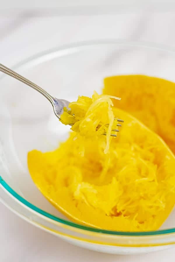 Large glass bowl filled with microwaved spaghetti squash. Fork pulling strands out of the bowl.