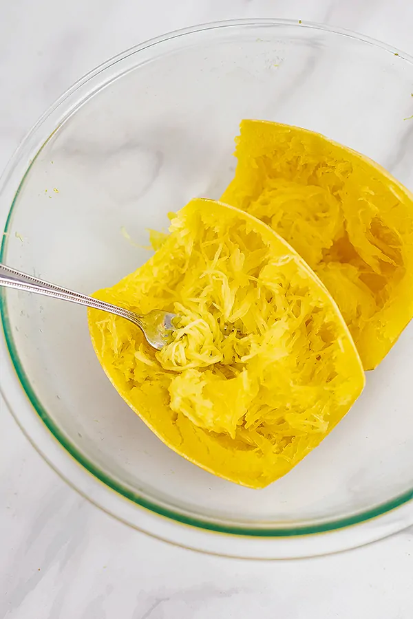 Large glass bowl filled with spaghetti squash, cut in half with a fork in the squash strands.