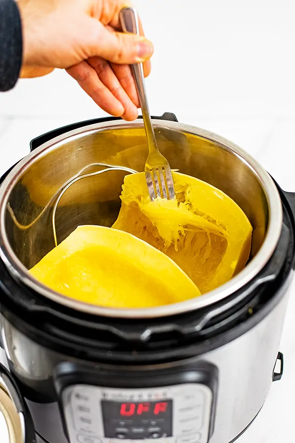 Pressure cooker filled with spaghetti squash. Fork is breaking up the strands of spaghetti squash