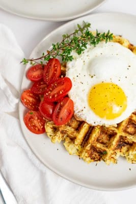 Overhead shot of parsnip savory waffle recipe topped with a fried egg, halved cherry tomatoes and thyme leaves