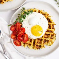 Overhead shot of parsnip savory waffle recipe topped with a fried egg, halved cherry tomatoes and thyme leaves