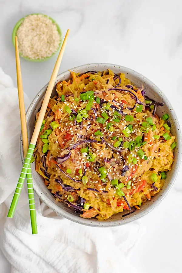 Overhead shot of a large bowl filled with vegan creamy Asian spaghetti squash recipe with chop sticks resting on the bowl and a bowl of sesame seeds in the background