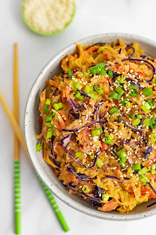 Overhead shot of a large bowl filled with vegan creamy Asian spaghetti squash recipe with chop sticks resting to the left of the bowl and a bowl of sesame seeds in the background