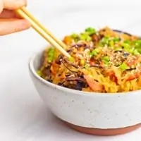 A large bowl with a rust colored bottom filled with creamy Asian vegan spaghetti squash recipe with chopsticks being held, plunging into the left side of the bowl