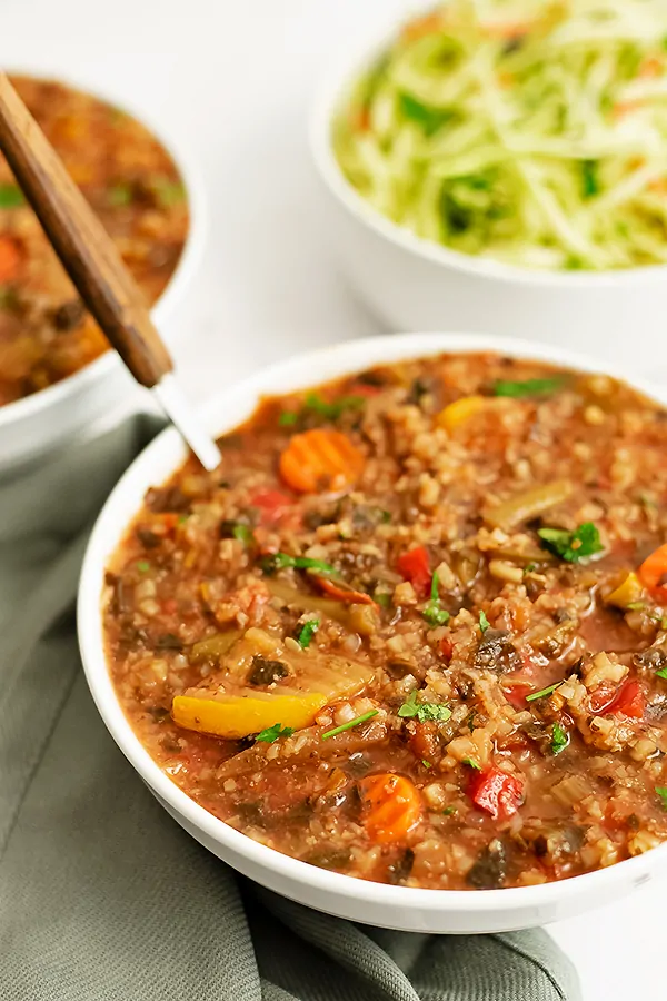 Large white bowl filled with crockpot low carb vegetable soup with a spoon with a wooden handle in the soup