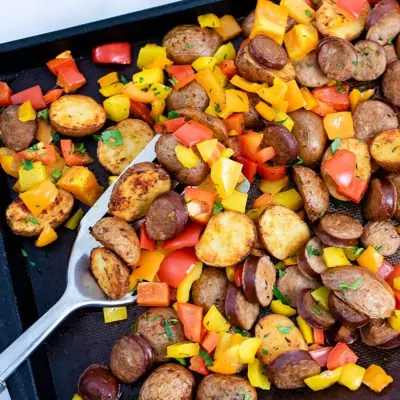 Sheet pan filled with easy tureky kielbasa and potatoes sheet pan dinner with a silver spatula in the center of the photo