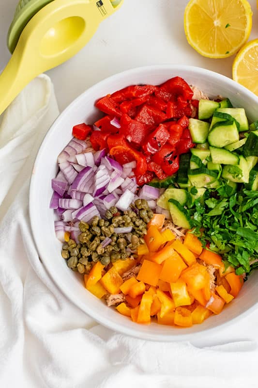 Large bowl filled with the ingredients for the healthy Mediterranean tuna salad (no mayo) before they have been stirred. Lemon juicer and lemons in the background