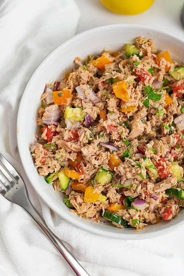 Overhead shot of a large bowl of healthy Mediterranean tuna salad (no mayo) with a fork to the right of the bowl and a lemon in the background