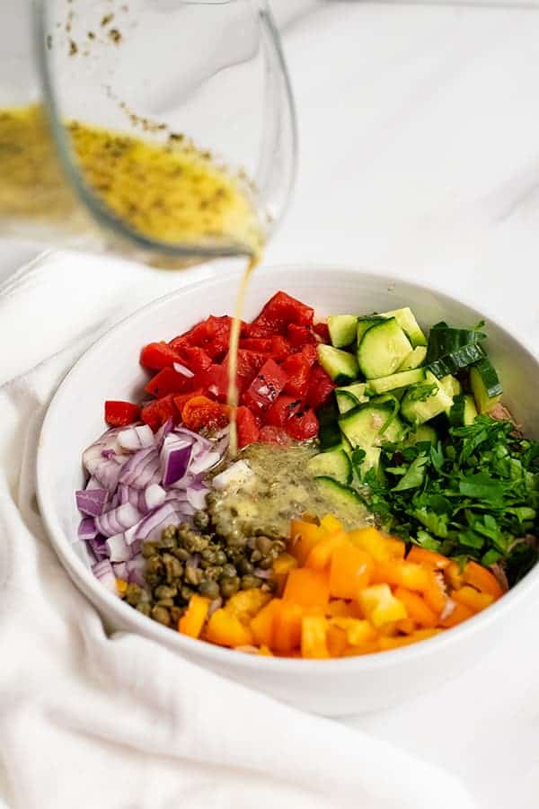 Lemon Herb Dressing being poured over the healthy Mediterranean tuna salad (no mayo) before it's been stirred