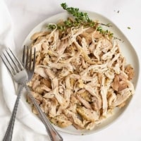 Overhead shot of a plate of Instant Pot Shredded Chicken Thighs with two forks on the left side of the plate and a white napkin