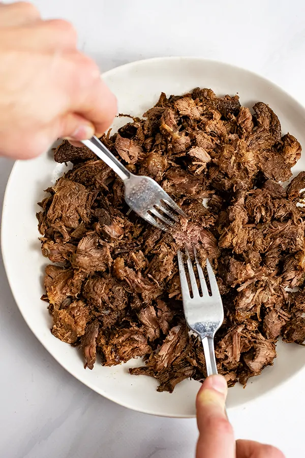 Two forks shredding the slow cooker balsamic beef