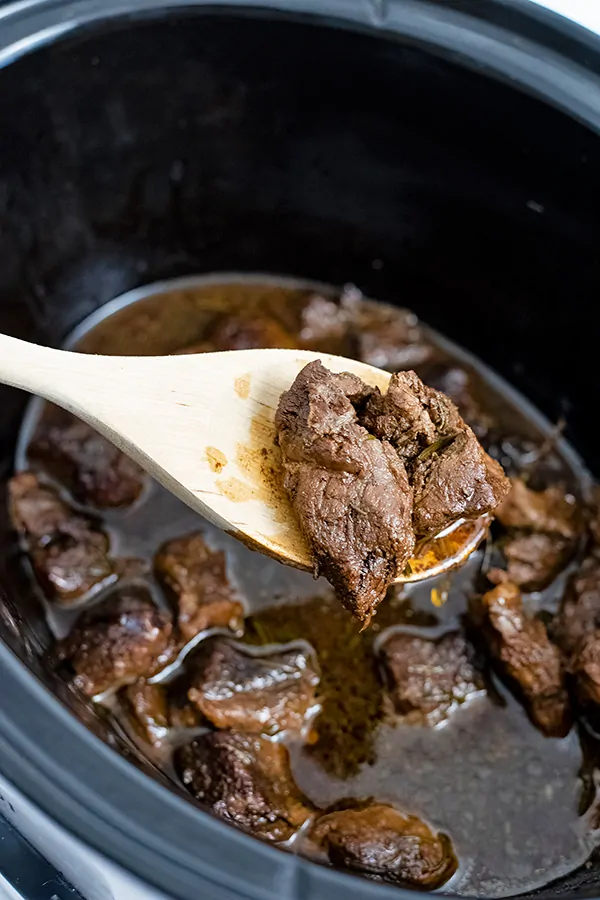 Large wooden spoon holding up a piece of the slow cooker balsamic beef over the slow cooker