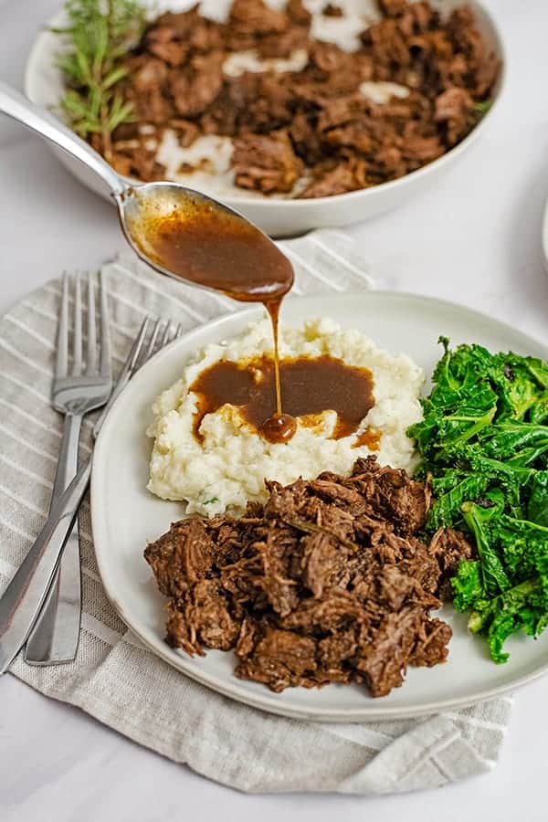 Dinner plate filled with slow cooker balsamic beef, mashed cauliflower, gravy and kale