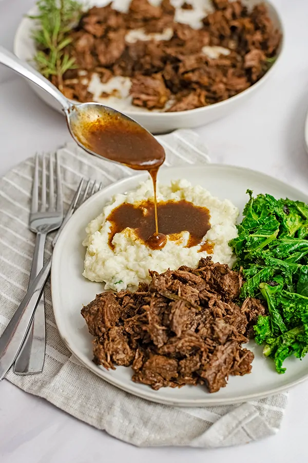 Dinner plate filled with slow cooker balsamic beef, mashed cauliflower, gravy and kale