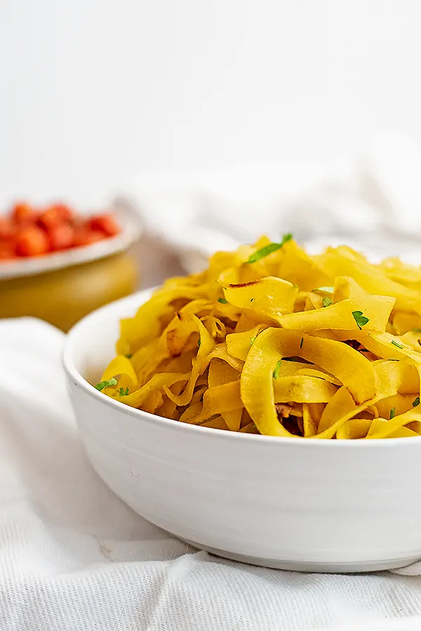 Large bowl filled with spiralized rutabaga recipe with a bowl of tomatoes in the background